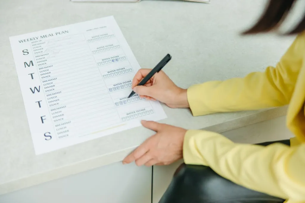 Person's hand with a black pen writing a meal plan.