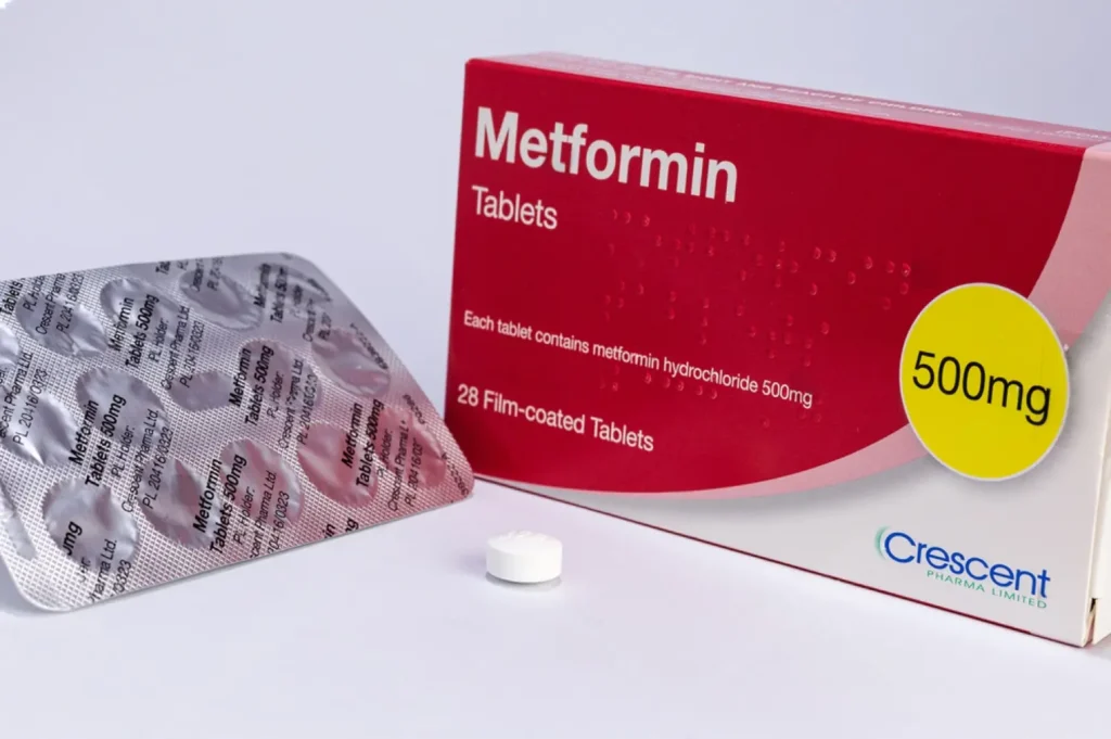 A box of metformin 500 mg tablets alongside a single tablet and blister pack all on a white surface.
