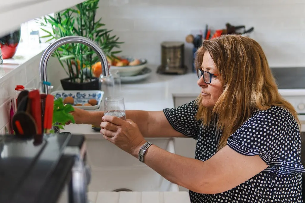 A Woman filling a glass with water in her home kitchen.