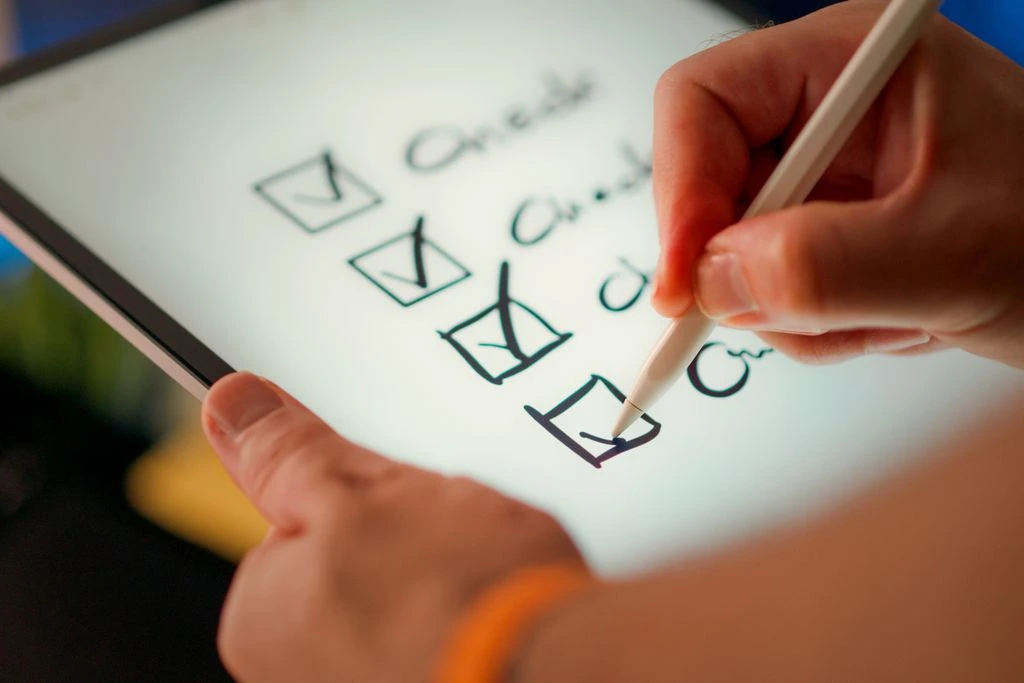 Close-up of a digital checklist being marked off on a tablet with a stylus pen.