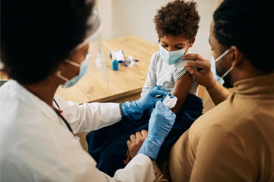 Doctor with a syringe in the right hand after injecting a toddler seated on their father's lap.