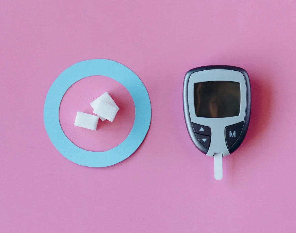 On the left, a cut-out of the universal blue circle symbol for diabetes with three sugar cubes in the middle, and a glucose meter on the right