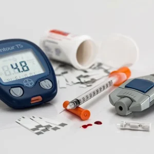 A glucose meter, blood lancet, test strips, drops of blood, insulin needle and syringe on a white surface