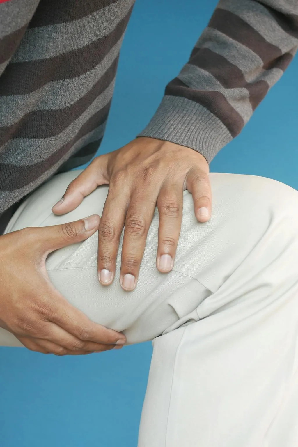 A closeup of a man holding his painful thigh.