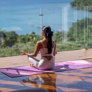 A woman seated on a purple mat in the lotus position.